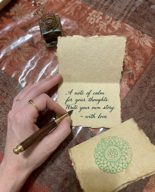 Hand writing on a piece of paper with a pen, surrounded by decorative elements on a textured surface.