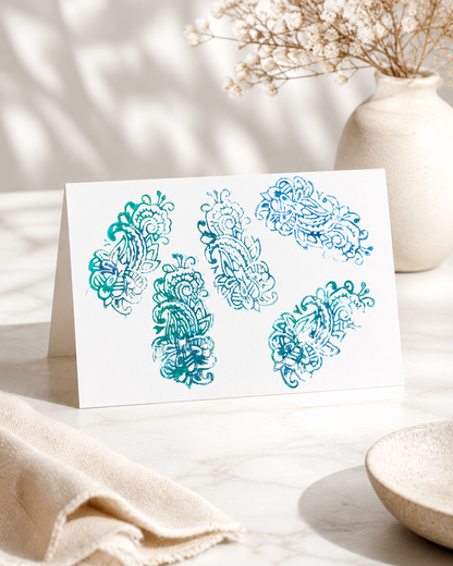 Card with blue floral designs on a light surface with a vase and fabric in the background