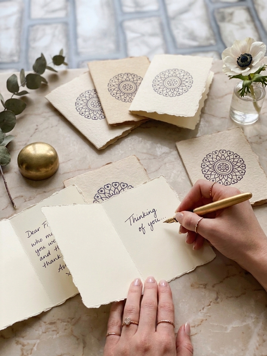 Person writing a card with decorative envelopes on a marble surface