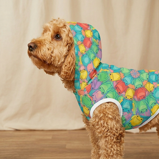 Dog wearing a colorful raincoat with a pattern of cartoon characters on a wooden floor.